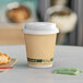 A brown EcoChoice paper hot cup with a white lid filled with coffee on a table with a croissant.