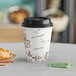 A Choice bean print paper hot cup with a lid and a croissant on a table.