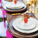 A table set with 10 Strawberry Street gold beaded rim glass charger plates and glasses with food.