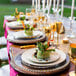 A table set with 12 10 Strawberry Street gold beaded rim charger plates and glasses of wine.