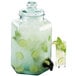 A Cal-Mil glass beverage dispenser with a drink inside and cucumbers and ice in it.