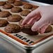 A hand holding a chocolate cookie over a SILPAT baking mat with more cookies.