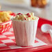 A white Genpak paper cup of macaroni and cheese on a red tray.