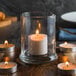 A Libbey glass votive holder with a lit candle inside on a table.