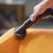 A hand using a Lavex dusting brush on a black tube attached to a vacuum cleaner.
