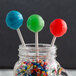 A blue lollipop on a Paper Lollipop Stick in a jar full of colorful candies.