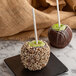 Two chocolate covered apples with nuts on Paper Pointed Candy Apple Sticks on a plate.