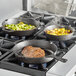 Three Valor pre-seasoned cast iron skillets cooking meat and vegetables on a stove.