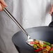 A person using a Town small wok spatula with a wood handle to stir vegetables in a wok.
