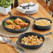 A group of Choice pre-seasoned cast iron skillets with fried chicken and potatoes on a table.