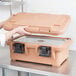 A woman holding a Cambro coffee beige top loading food pan carrier with a lid.