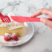 A hand holding an Eco-Products coral compostable plastic knife and fork over a piece of cake.