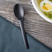 A black Eco-Products compostable plastic spoon in a bowl of soup on a table.