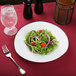 A CAC Sushia triangular porcelain salad plate with a salad, fork, and glass of water on a table.