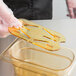 A plastic gloved hand uses a Carlisle amber high heat drain tray over a clear plastic container.