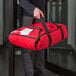 A person holding a red Cambro insulated pizza delivery bag.