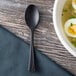 A bowl of soup with eggs and broth next to a black Eco-Products compostable plastic spoon.