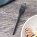 A black Eco-Products compostable plastic fork on a wood surface next to a plate of food.