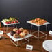 An Acopa stainless steel display stand set with trays of muffins on a table.