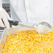 A person in white gloves using a Vollrath black perforated oval spoodle to serve corn.