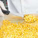A person in white gloves using a Vollrath black perforated oval Spoodle to scoop corn into a container.