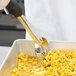 A person using a Vollrath black perforated oval Spoodle to scoop corn into a pan.