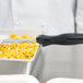 A chef using a Vollrath black perforated oval Spoodle to serve food from a metal container.