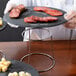 A round metal Choice display stand with a plate of cheese and sliced meats on a wood table.