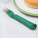 A fork and knife on a white plate with a Hunter green napkin wrapped around the fork.