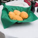 A Hunter green linen-like napkin with a basket of bread rolls on a table.