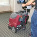 A person using a Minuteman X17 carpet extractor on a carpet in a corporate office cafeteria.