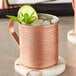 An Acopa hammered copper mug with ice, lime, and mint leaves on a table.