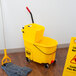 A Rubbermaid yellow mop bucket with a mop on the floor.