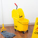 A Rubbermaid yellow mop bucket with a down press wringer next to a yellow caution sign.