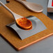A Tablecraft brushed stainless steel square spoon rest with a wooden spoon on it.