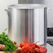 A Choice aluminum stock pot with lobsters and vegetables on a stove.