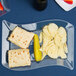 A clear plastic luncheon plate with a sandwich and chips on a table.