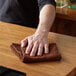 A hand using a brown Choice textured terry bar towel to wipe a table in a bar.