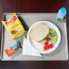 A Cambro taupe dietary tray with a sandwich, chips, and a drink on it.
