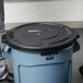 A blue Rubbermaid trash can with a black lid.