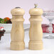A wooden salt shaker and pepper mill with a natural finish on a table.