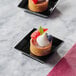 Two small black square plastic trays with desserts on a table.