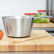 A Vollrath stainless steel sauce pan on a wooden surface with a spoon inside.