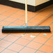 A Carlisle Sparta Spectrum push broom head with black and blue unflagged bristles on the floor.