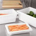 A white Rubbermaid food storage container on a counter with carrots and peppers in it.