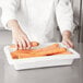 A person picking up carrots in a Rubbermaid food storage box.