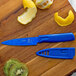 A Mercer Culinary blue non-stick paring knife with a sheath cutting a lemon on a wood cutting board.