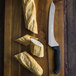 A Dexter-Russell Scalloped Offset Sandwich Knife cutting sliced bread on a cutting board.