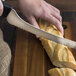 A person using a Dexter-Russell Scalloped Offset Sandwich Knife to cut a loaf of bread.