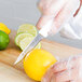 A person in a plastic glove uses a Dexter-Russell white paring knife to cut a lemon.